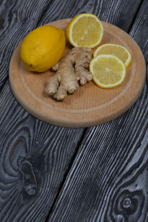 Lemon and ginger on a cutting board. The lemon is cut into slices. Against a background of black pine boards.の写真素材