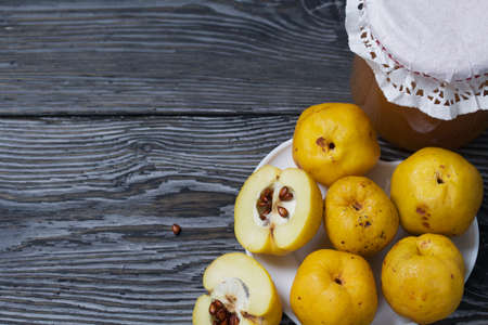 Quince fruits on a plate. Quince jam. The yellow fruit is cut, the seeds are visible. Plate on black pine boards. Close-up shot.の写真素材