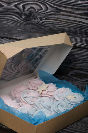 Marshmallow blue and pink. Lies in craft packaging. Decorated with mastic snowflakes. On black pine...