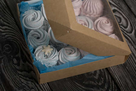 Marshmallow blue and pink. Lies in craft packaging. Decorated with mastic snowflakes. On black pine boards.の写真素材