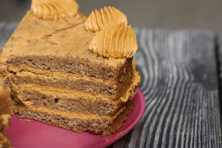 Banana cake with butter cream. Lies on a plate, cut into pieces. On black pine boards. Close-up...