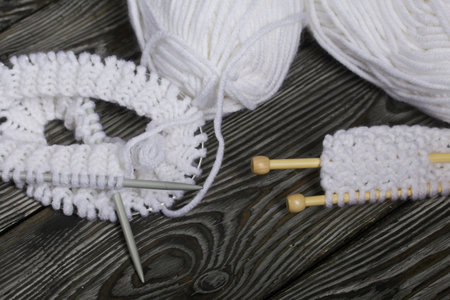 Knitting with needles. A skein of white thread and a fragment of a knitted product. On black pine...