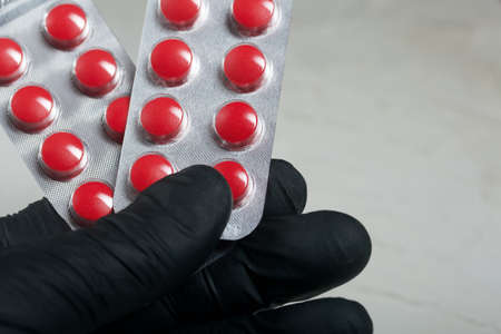 Blisters with red pills in a hand in a rubber glove. On a light background. Close-up.
