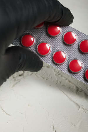 Blisters with red pills in a hand in a rubber glove. On a light background. Close-up.