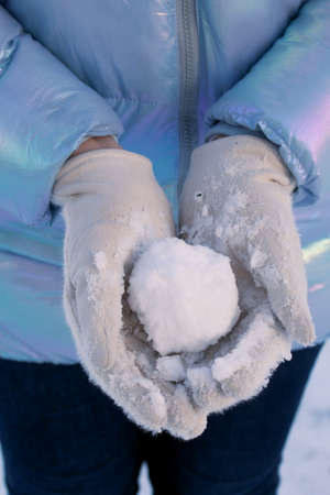 A woman in white winter gloves holds a snowball. On a walk in the winter park. close-up.の写真素材