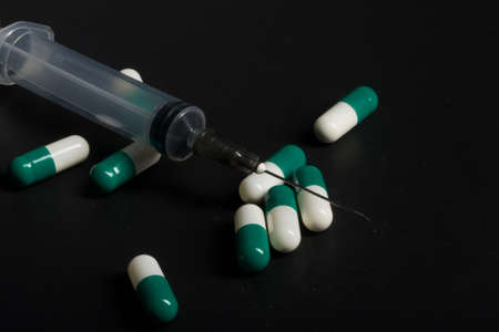 Pills are white-green. medical syringe. Symbol of drug addiction. On a black background.の写真素材
