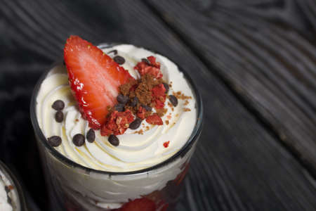 Dessert of strawberries with cream. In a glass jar. On black pine boards. close-up.