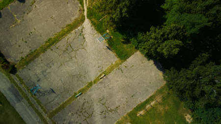 An old school stadium in a city block. Cracked asphalt and sports equipment. Multi-storey buildings and a large green area. aerial photography.の写真素材