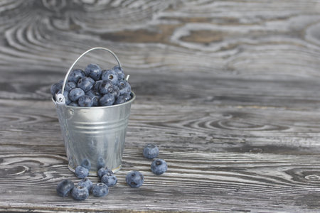 Ripe blueberries in a metal bucket. On pine boards. Several berries are scattered around. close-up.の写真素材
