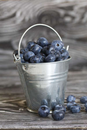 Ripe blueberries in a metal bucket. On pine boards. Several berries are scattered around. close-up.の写真素材