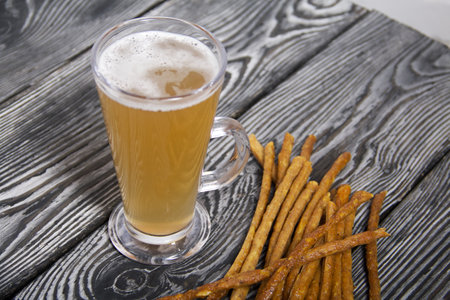 Thin sausages for beer. Nearby is a glass of wheat beer. background from pine boards. close-up.の写真素材