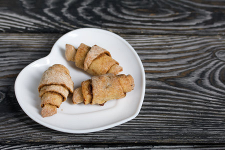 Croissants with cinnamon. Rolls with cinnamon. They lie on a saucer. Background from black pine boards. Shot close-up.の写真素材