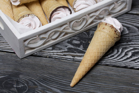 Wafer cones filled with marshmallows. Packed in a wooden tray. Several copies are stacked nearby. Homemade marshmallow. On pine boards. Taken from above.の写真素材