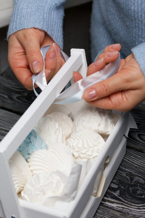 Marshmallow cones. homemade zephyr. Packed in a wooden decorative box. A woman ties a ribbon into a bow. On the background of the boards. close-up.の写真素材