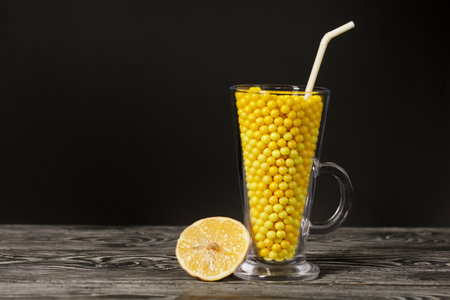 The glass goblet is filled with vitamins in the form of dragees. Next to a slice of lemon. On black pine boards. On a black background.の写真素材