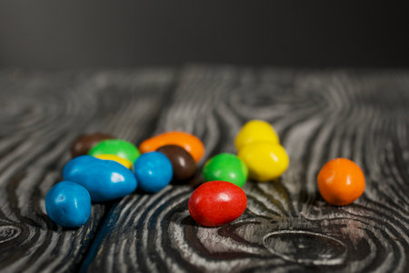 Chocolate candy in multi-colored glaze. Scattered on black pine boards. close-up.の写真素材