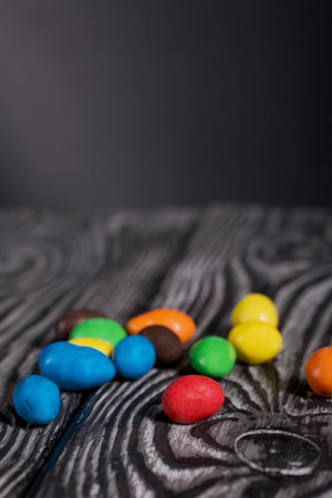 Chocolate candy in multi-colored glaze. Scattered on black pine boards. close-up.
