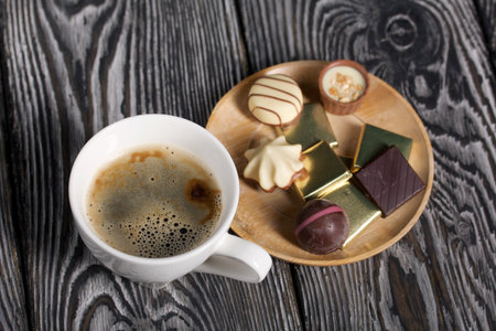 A cup of black coffee in a white cup. Chocolate in foil and chocolates. On pine boards.の写真素材