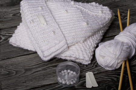 Knitted hat and scarf in white. Women's handmade knitted clothes. Nearby is a skein of white thread...