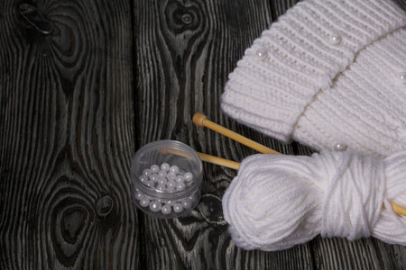 Knitted scarf in white. Women's handmade knitted clothes. Nearby is a skein of white thread for knitting and knitting needles. On black boards.の写真素材