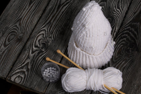 Knitted scarf in white. Women's handmade knitted clothes. Nearby is a skein of white thread for knitting and knitting needles. On black boards.の写真素材