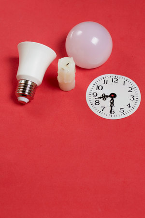 Disassembled LED bulb. Nearby is a candle stub. Clock face with arrows at 20:30. Global ecology,...