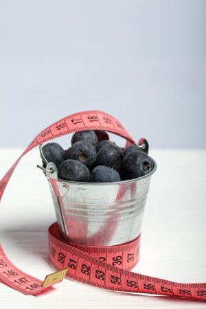 Large blueberries in a decorative bucket. Measuring tape for measuring the waist. International day without diets. On a white background. close-up.の写真素材