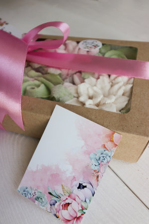 Homemade marshmallows in a paper gift box. Zephyr flowers. The box is tied with a ribbon tied into a bow. Label for the text. Near the congratulatory postcard. Close-up.の写真素材