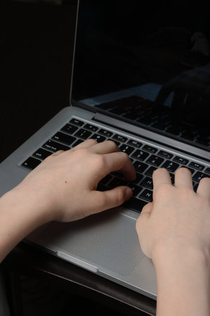 Detailed close-up of a teenager's palms over a laptop keyboard, showing their technological...
