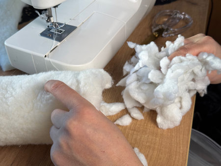 A woman is putting stuffing into the sewn piece. She is sewing a pet bed from fur fabric. Close-up.の写真素材