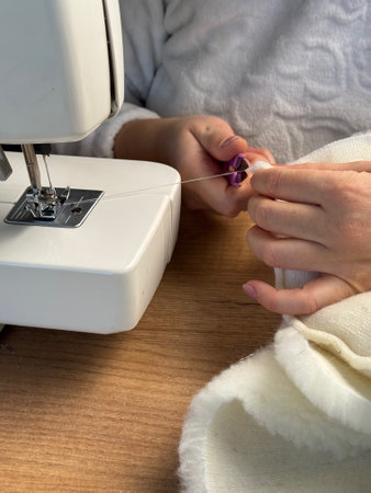 The woman cuts the thread with scissors. She is sewing a pet bed from fur fabric.の写真素材