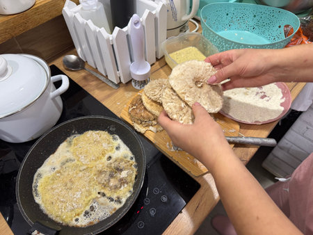 A woman fries breaded umbrella mushrooms. She holds mushroom caps in her hands.の写真素材