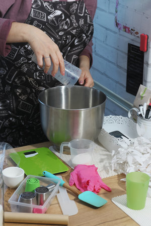 A woman pours water into the bowl of a planetary mixer. Nearby on the table are tools for making...