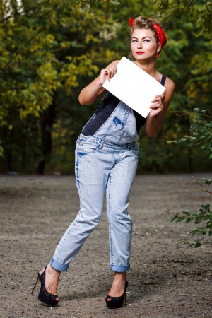 Beautiful pin-up girl in denim overalls and a red bandana holding copyspaceの写真素材