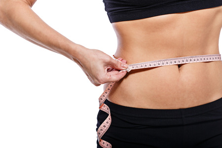 Girl measuring waist circumference after a grueling workout, isolated on white backgroundの写真素材
