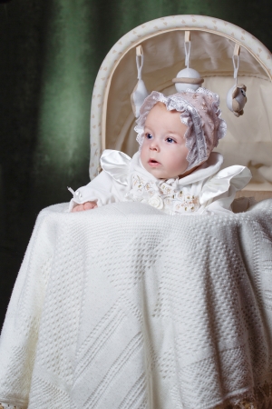 Cheerful and happy blue-eyed baby in  bonnet lies in cradleの写真素材