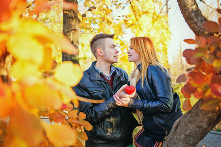Young couple holding a red heart standing between trees autumn parkの写真素材