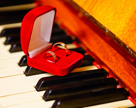 Wedding rings in a red box standing on the piano keys closeup shotの写真素材