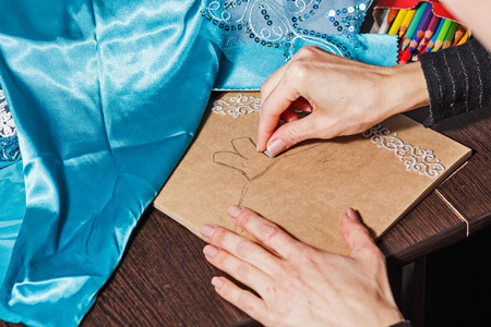 Fashion designer draws a sketch of the future dress on paper, beside lie thread and lace