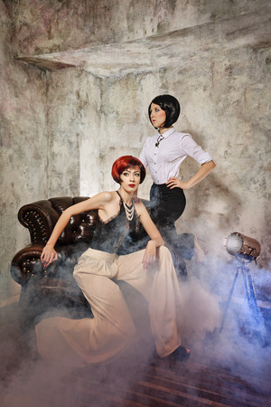 Two young attractive girls posing on a leather chairの写真素材