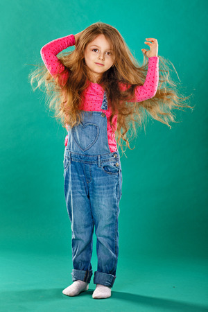 Portrait of a little girl with long curly hair in denim overallsの写真素材
