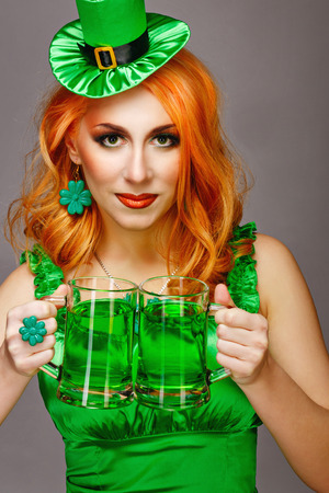 Red hair girl in Saint Patrick's Day leprechaun party hat having fun, holding a mug of aleの写真素材