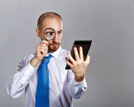 Businessman in shirt and tie looking through a magnifying glass on a tablet PC. Business people. Concept of success.の写真素材