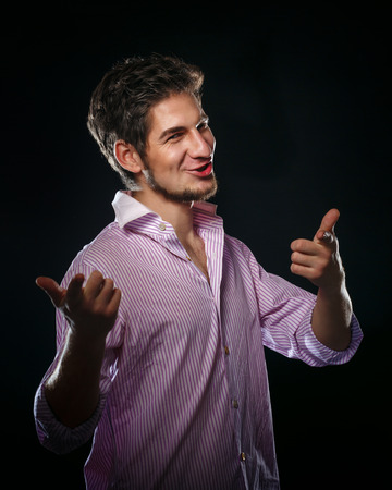 Portrait of a young man on a black background in the studio. The man smiles and shows finger. A man wearing a shirt.の写真素材