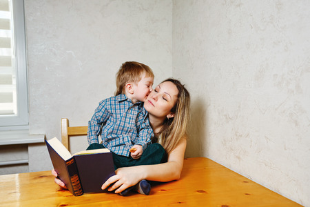 Mother and son reading a book. Mother holding a book hugging son. Boy kisses his mother. Happy family leisure.の写真素材