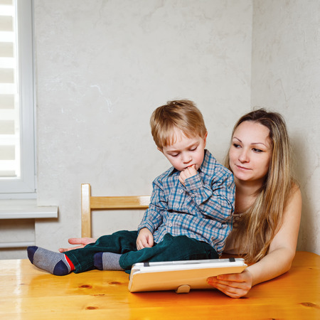 Mother and child play on a Tablet PC in the nursery. Family leisure, modern, young and technology.の写真素材