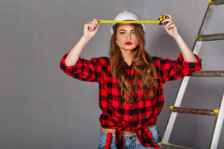 Attractive girl builder holding a tape measure. Girl dressed in jeans, a plaid shirt and a helmet. Concept of building and architecture.の写真素材