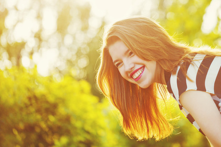 Girl smiling portrait in the city park. Shooting at sunset. Sun glare in the frame. Walk. The concept of street fashion.の写真素材