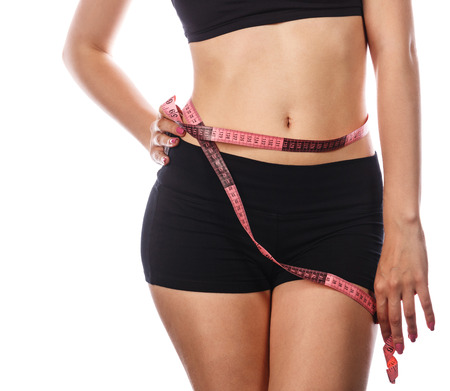 Young slim woman measuring waist circumference, after a diet. Isolated on white background. The concept of excess weight loss and healthy eating.の写真素材