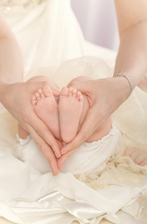 A young mother holding her daughter\\\'s feet. Hands folded in the shape of a heartの写真素材